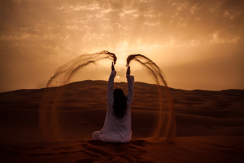 Mulher sentada no deserto enquanto joga areia durante a hora dourada