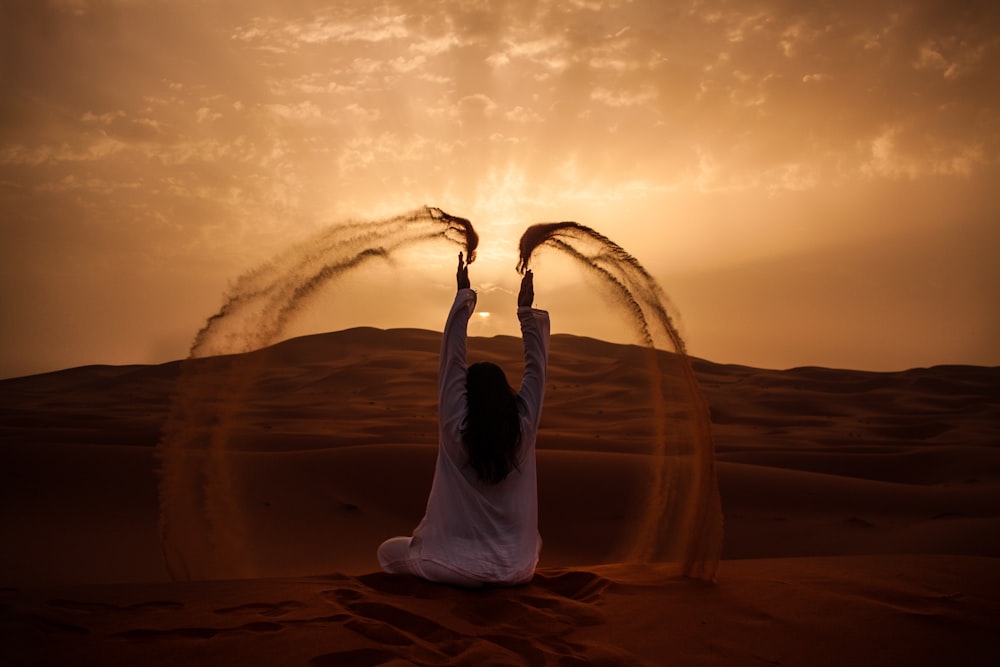 황금 시간 동안 모래를 연주하면서 사막에 앉아있는 여자