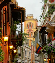 A narrow street with colonial buildings and a yellow church tower in Cartagena, Colombia