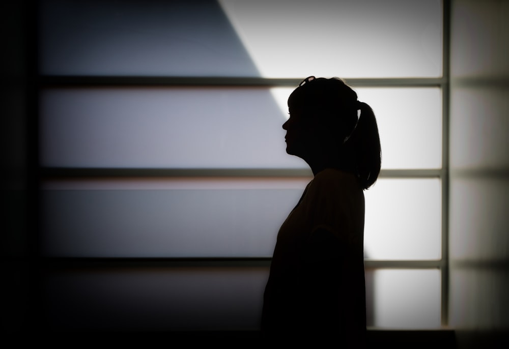 silhouette photo of woman standing near white framed glass window