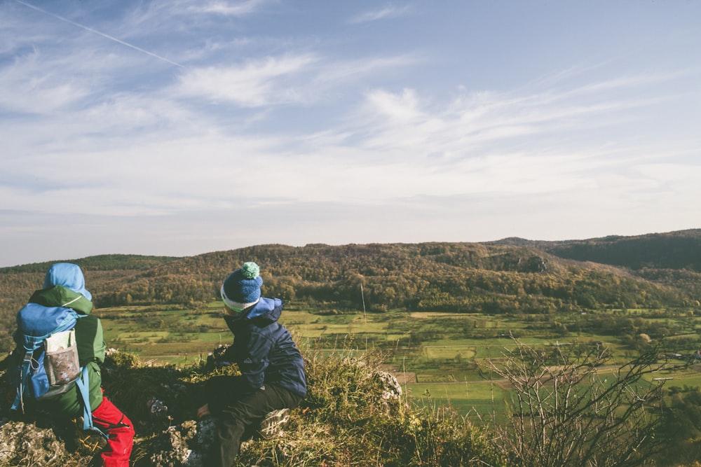 two person sitting on rock near mountain