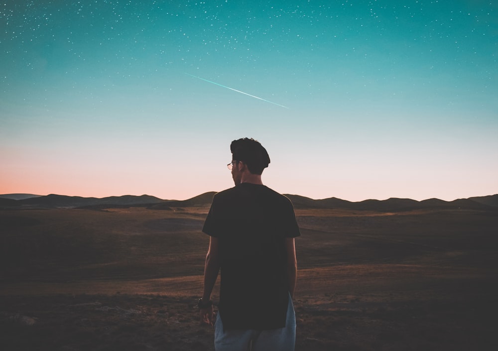 man wearing black top standing in front of mountain