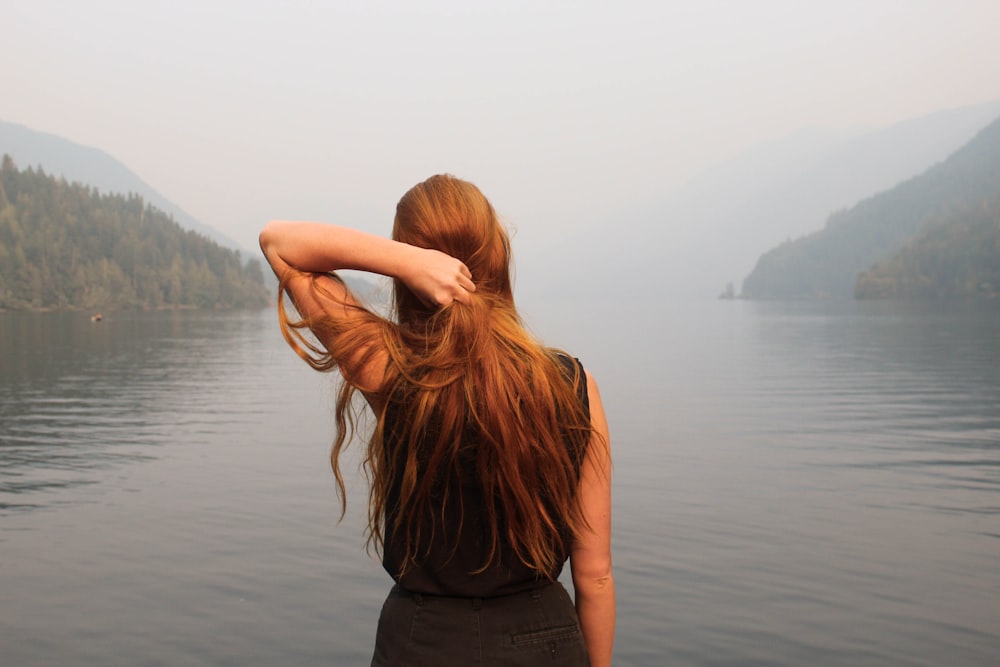 mujer sosteniendo el cabello mirando hacia el cuerpo de agua durante el día