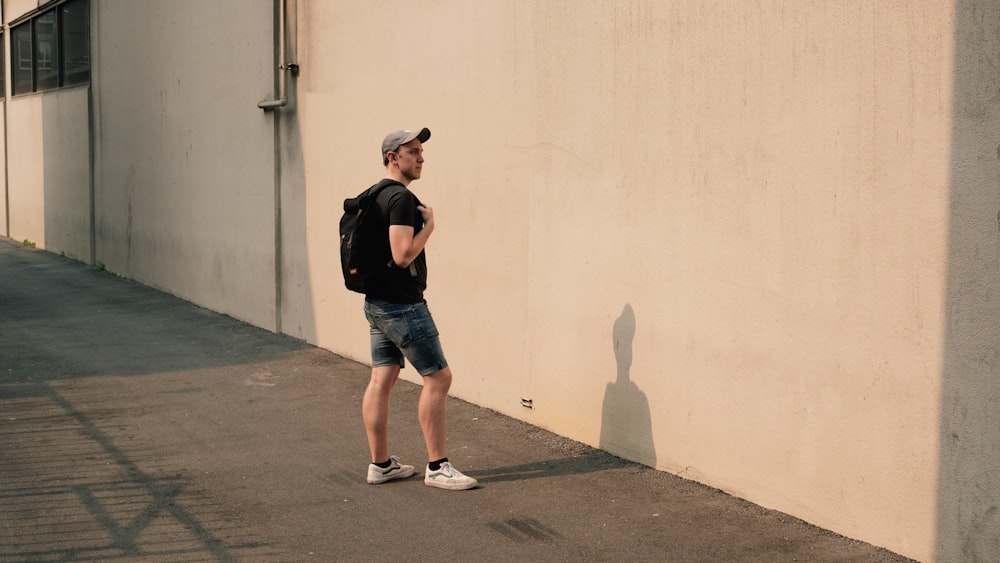 man standing beside white concrete wall