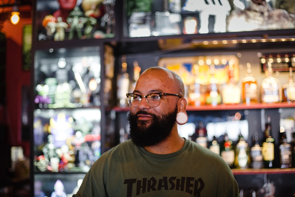 man in gray Thrasher crew-neck shirt standing near rack of bottles