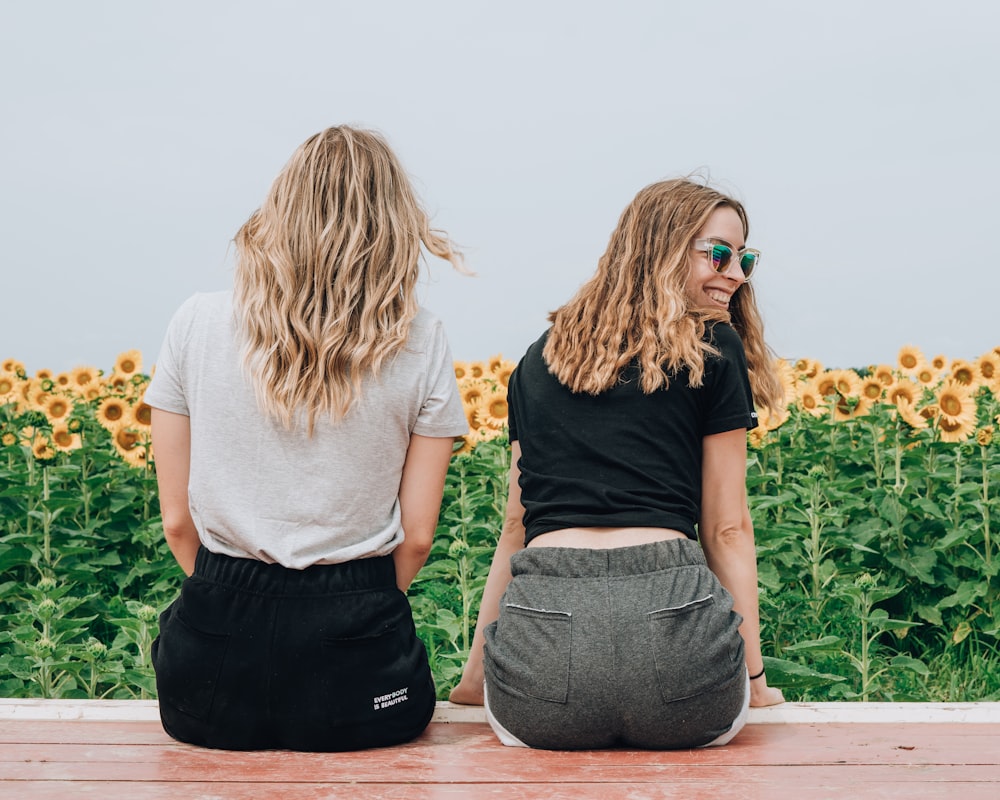 two women's sitting in front of sunflowers