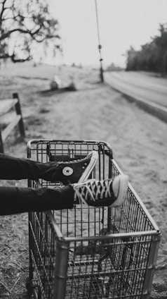 grayscale photo of person foot on metal grocery cart