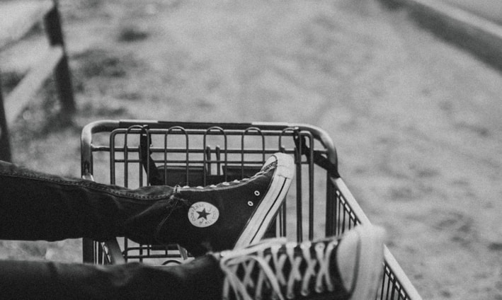 grayscale photo of person foot on metal grocery cart