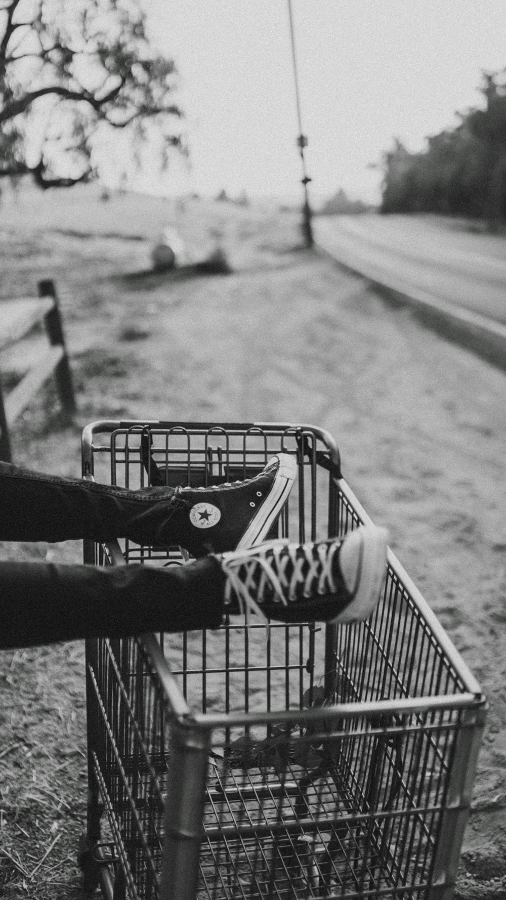 foto em tons de cinza do pé da pessoa no carrinho de supermercado de metal