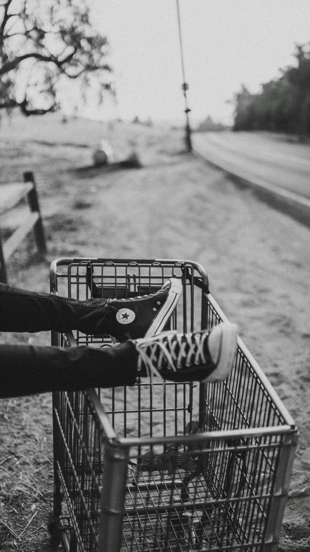 Foto en escala de grises del pie de la persona en el carrito de la compra de metal