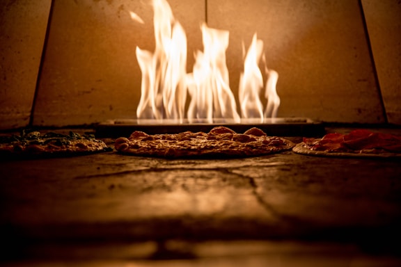 Cozy artisanal pizza oven with hand-crafted pizzas baking inside in a warm, inviting restaurant setting.