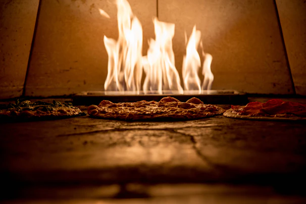 A close-up of a wood-fired pizza oven glowing warmly with flames licking the crust of a pizza.