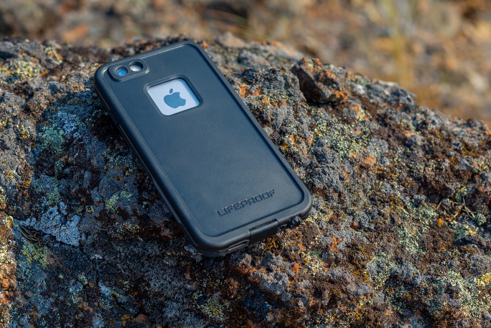 iPhone with black Lifeproof case on rock during daytime