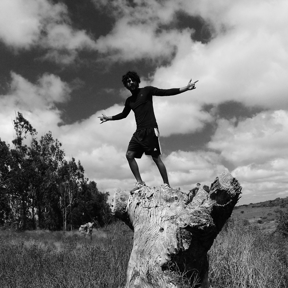 grayscale photo of man standing near tree under cloudy sky