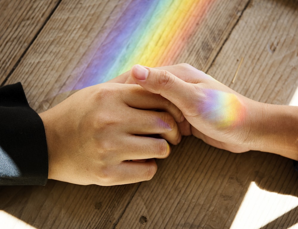 two holding hands on table with rainbow