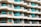 A modern multi-story apartment building with an array of balconies featuring glass railings and turquoise curtains. The building has a repetitive geometric pattern with each balcony offering a semi-circular shape and light fixtures on the walls. The façade is painted in balanced tones of beige and light brown.