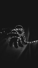 A hand is entangled with glowing LED strip lights set against a dark background. The lights create a stark contrast, accentuating the curves of the hand and the delicate illumination of the LEDs.