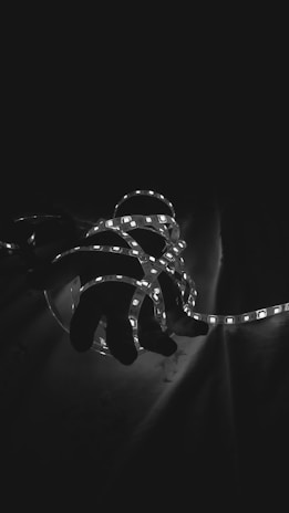 A hand is entangled with glowing LED strip lights set against a dark background. The lights create a stark contrast, accentuating the curves of the hand and the delicate illumination of the LEDs.