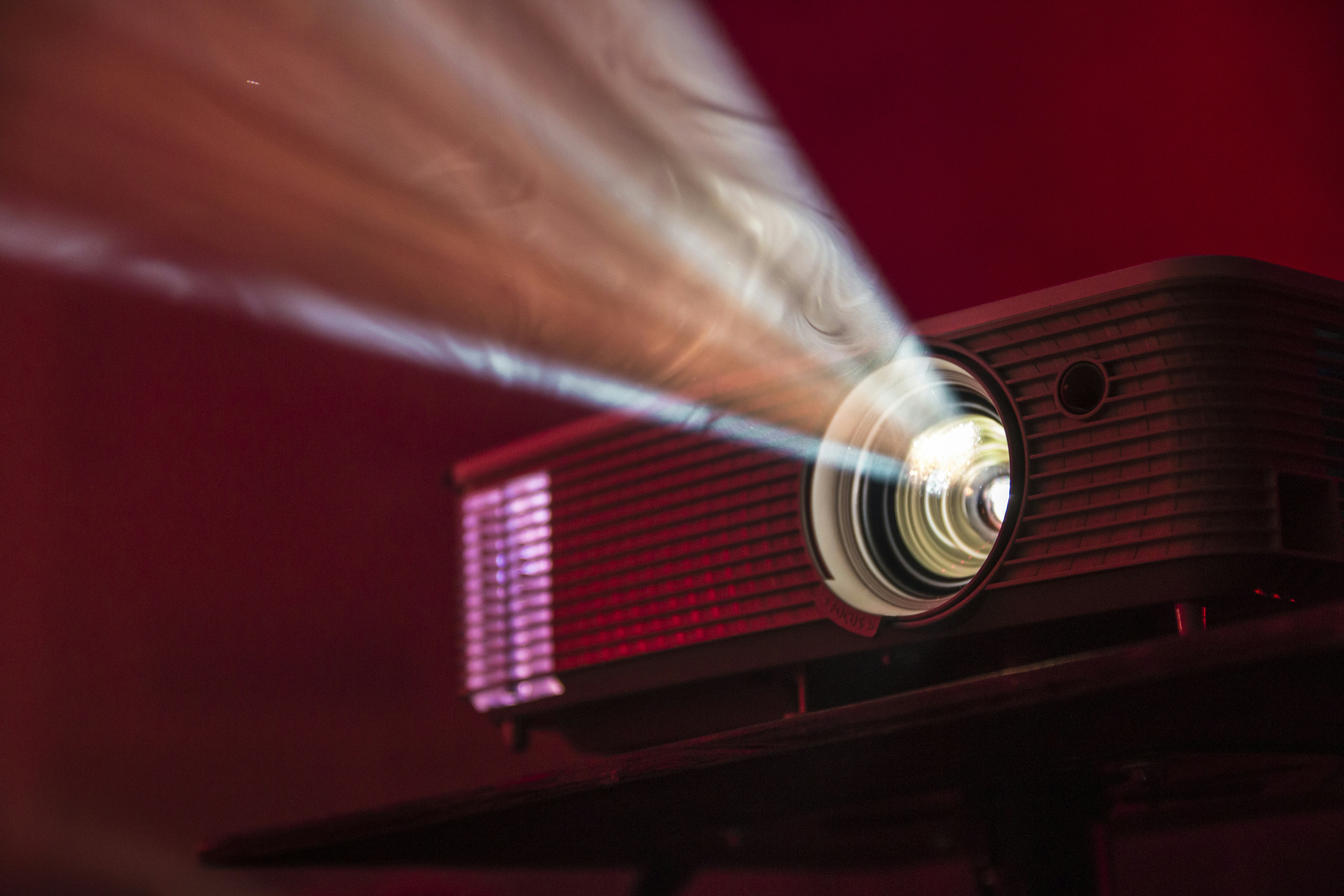 A projector shines the white light of an image against a dark maroon background.