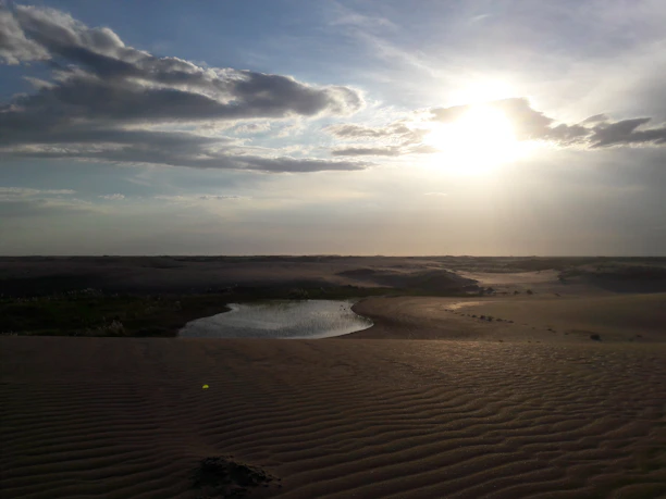 A serene sunrise over the golden dunes of Sharqiya Sands, with a luxury desert camp in the distance.