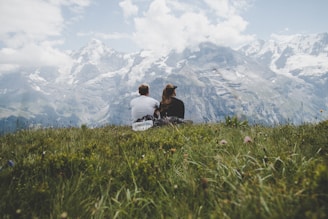 man sitting beside woman on grass facing mountains