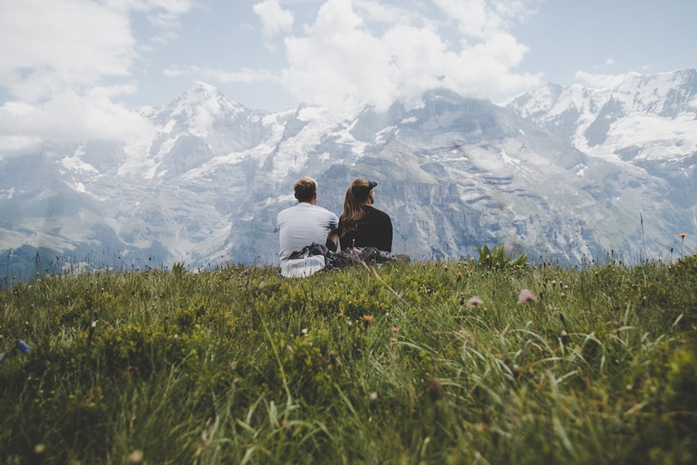 man sitting beside woman on grass facing mountains