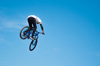 A vibrant BMX rider mid-air performing a trick against a clear blue sky backdrop.