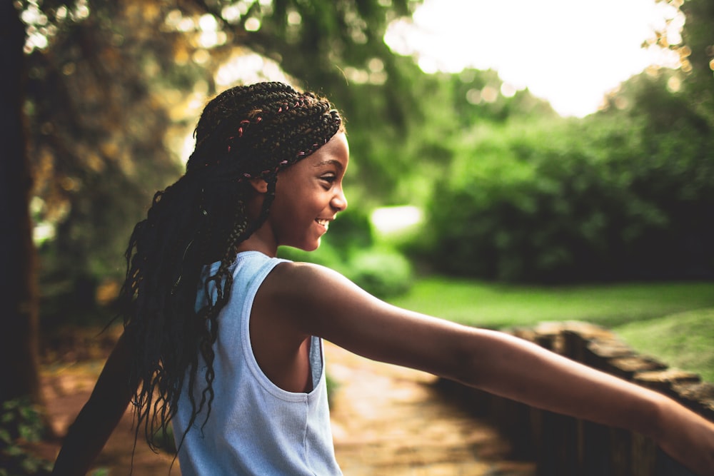 shallow focus photography of girl in white tank top near tree during daytime