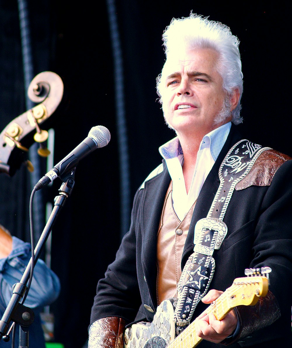 man playing guitar in front of microphone during daytime