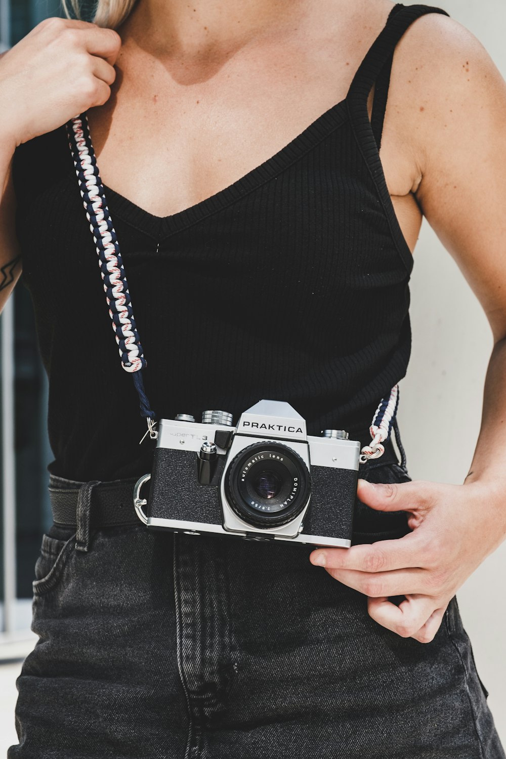 mujer con camisola negra de correa de espagueti sosteniendo una cámara Praktica SLR negra y gris