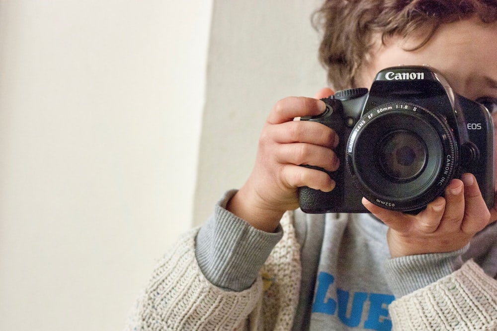 garçon tenant un appareil photo reflex numérique Canon