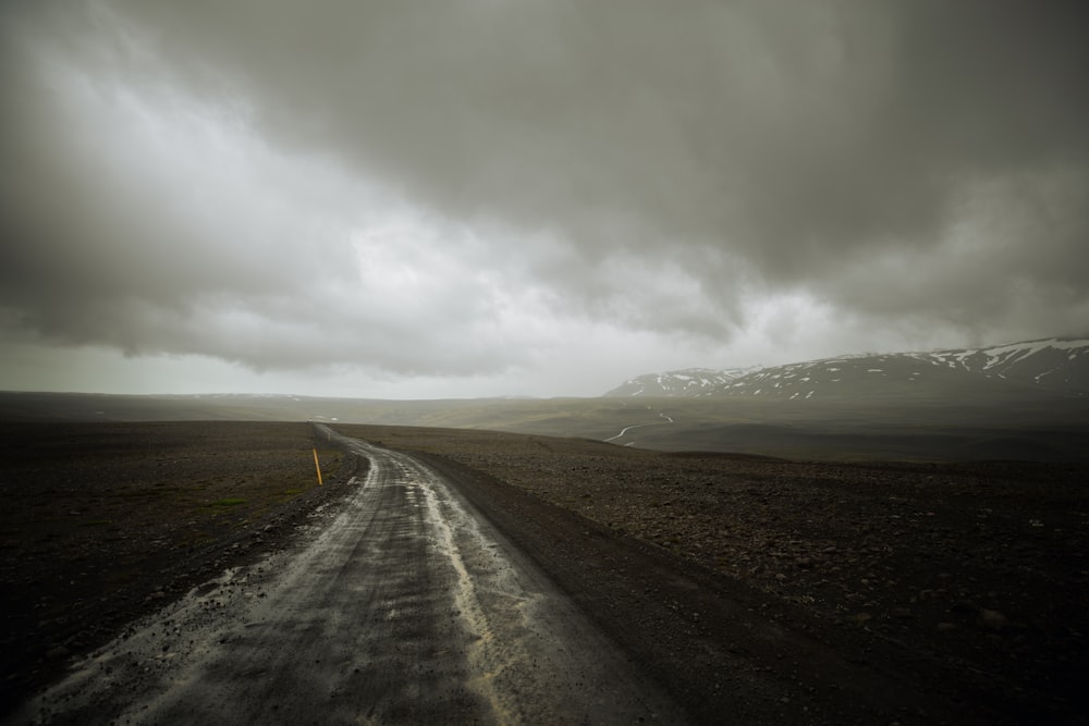 landscape photography of road between grass field under gray sky