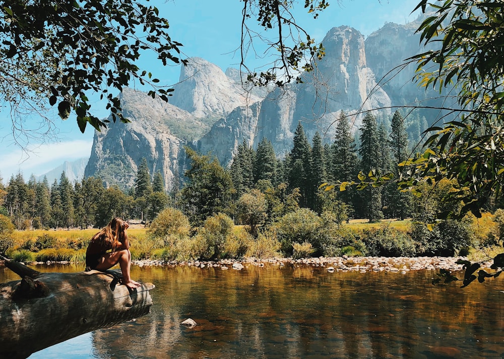 woman sitting on wood near body of water