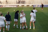 Women playing football together on a sunny outdoor field, smiling and active.