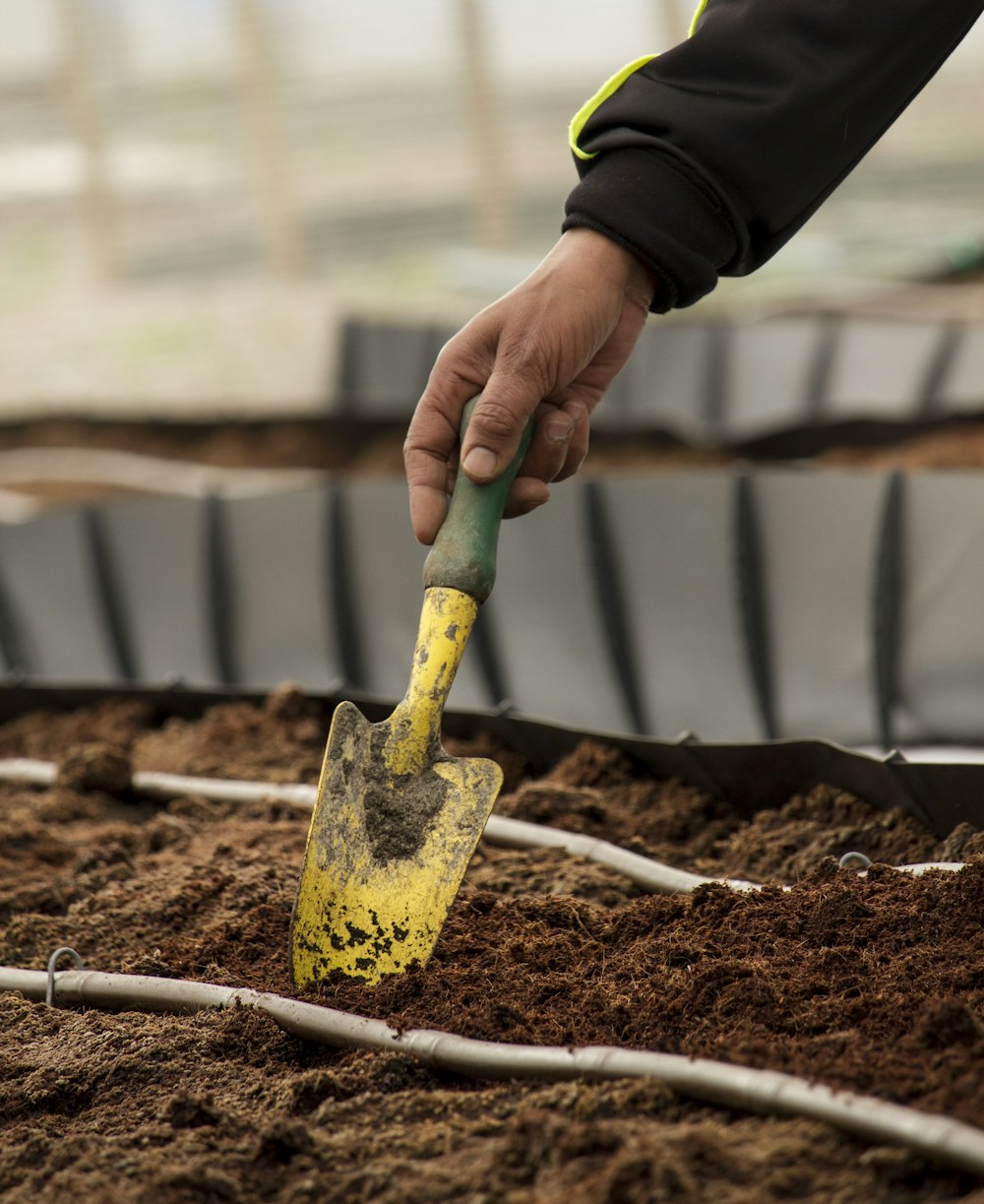 personne tenant une pelle de jardinage jaune et verte