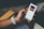 A person holds a smartphone displaying a music app interface. The screen shows a song titled 'Furious' by Jade Bird. The individual's hand is adorned with a white perforated watch band. The background includes a wooden armrest and a blurred pair of shorts.