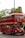 A classic red double-decker bus with signage for a wedding party is parked on a street. The bus is decorated with ribbons and has a sign that reads '2018 Happy Wedding Day' above the windshield. It is surrounded by greenery and trees in the background.