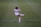 A female soccer player in a white uniform is kicking a ball on a green soccer field. The player has dark hair tied back and is focused on the action. The uniform has a prominent logo, and the player is wearing white socks and cleats with red accents.