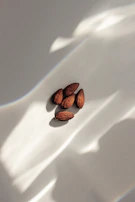 Natural light casting soft shadows over a handful of almonds and cashews on a light wood table.