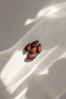 Natural light casting soft shadows over a handful of almonds and cashews on a light wood table.