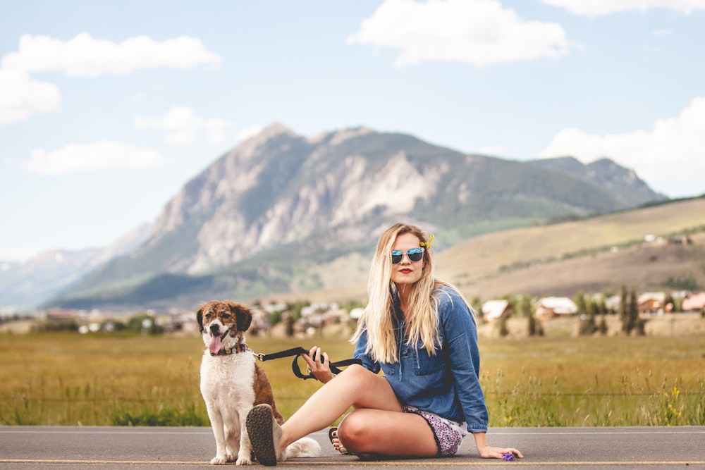 a woman sitting on the side of a road next to a dog