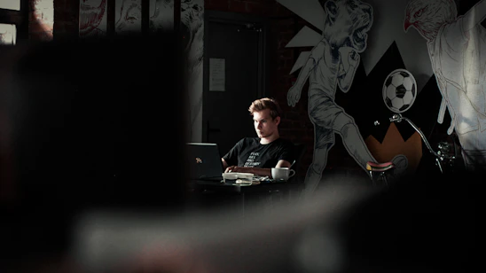 A welcoming young person working on a laptop surrounded by notes and a cup of coffee, symbolizing creativity and entrepreneurship.