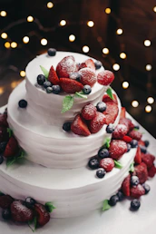 close-up photography of 3-tier vanilla cake with blueberry and strawberry toppings