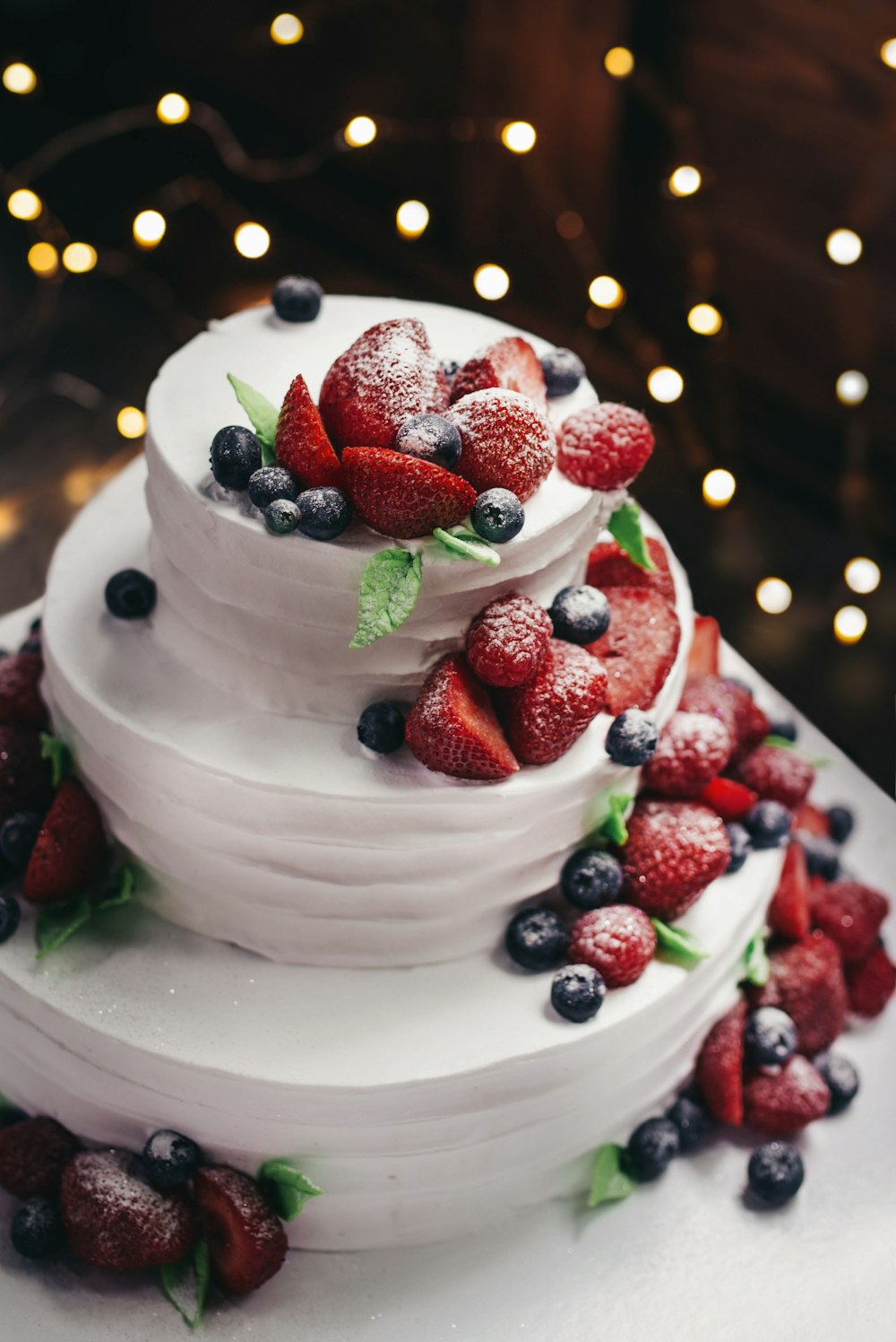 Fotografía de primer plano de pastel de vainilla de 3 niveles con coberturas de arándanos y fresas