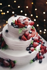 close-up photography of 3-tier vanilla cake with blueberry and strawberry toppings