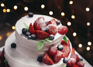 close-up photography of 3-tier vanilla cake with blueberry and strawberry toppings
