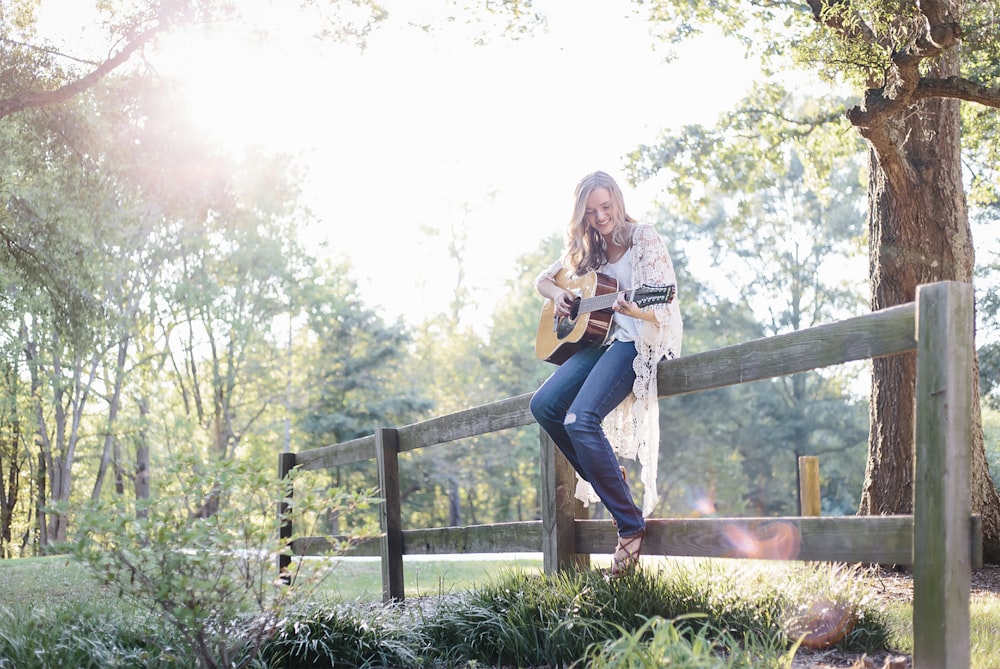 woman sitting on fence while playing guitar