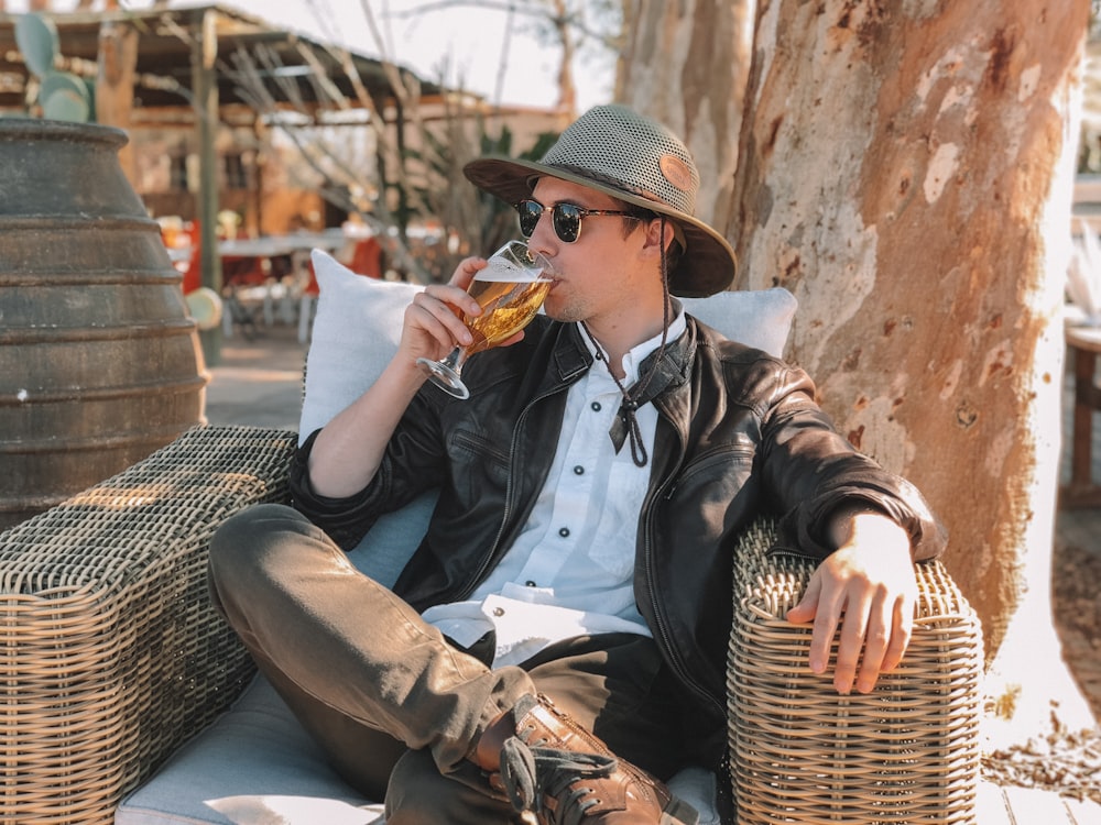 man in black leather jacket and brown pants sitting on blue wooden bench during daytime