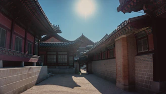 A traditional Korean architectural complex bathed in sunlight, featuring intricately designed roofs and brick walls. The courtyard is empty, creating a sense of calm and serenity.