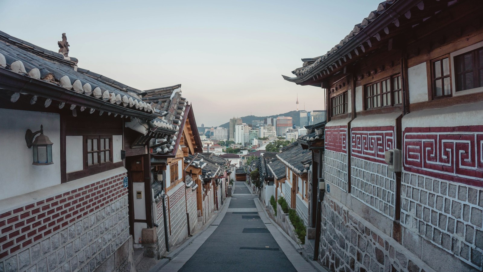 A quiet lane of traditional hanok houses in Seoul's Bukchon area, with the modern city skyline beyond